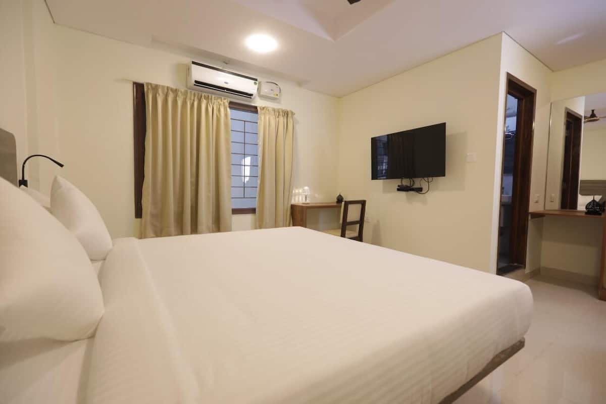 Habitación de hotel con una cama grande, un equipo de aire acondicionado, un televisor montado en la pared y una ventana con cortinas.