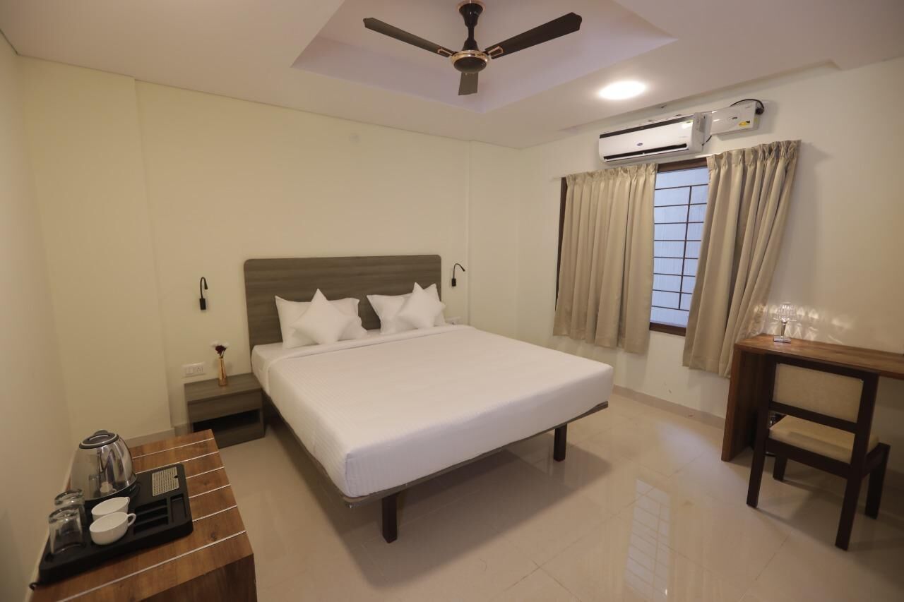 A hotel room with a bed, bedside tables, a ceiling fan, an air conditioning unit, and a window with curtains.