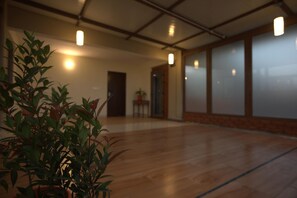 A spacious room with wooden flooring, a potted plant in the foreground, and a door leading to another room. - BLU THE HOTEL (Bengaluru)