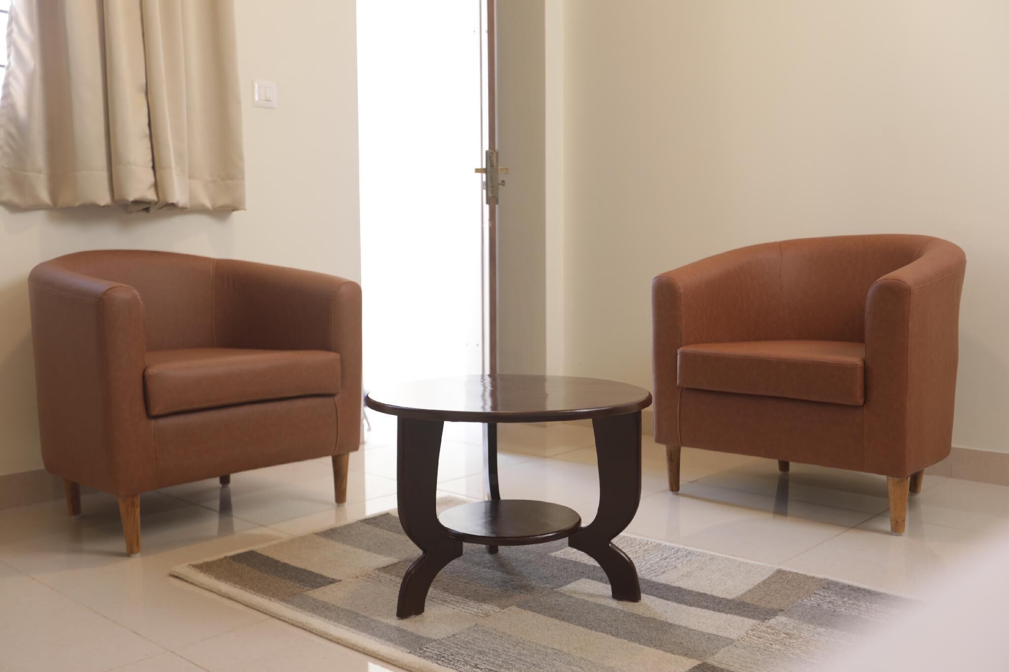A room with two brown armchairs, a small round table, and a patterned rug.