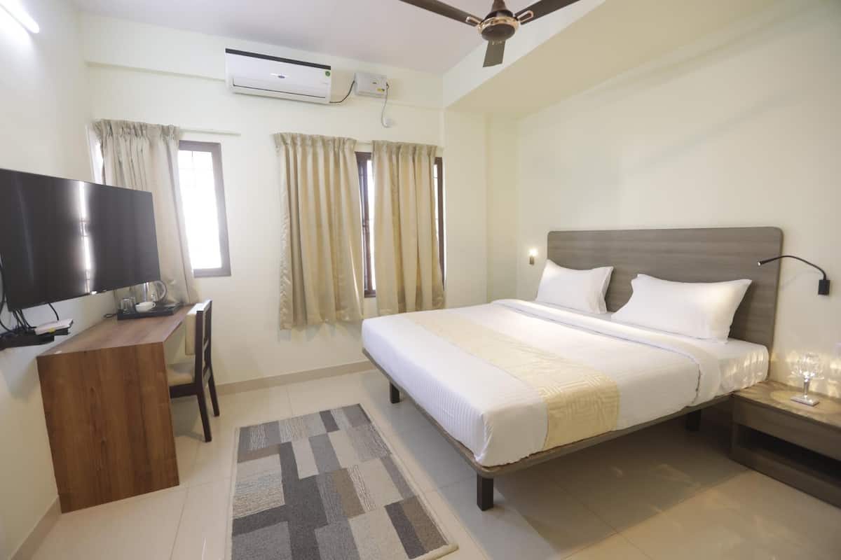 Una habitación de hotel con cama, escritorio con televisor, ventilador de techo y cortinas.
