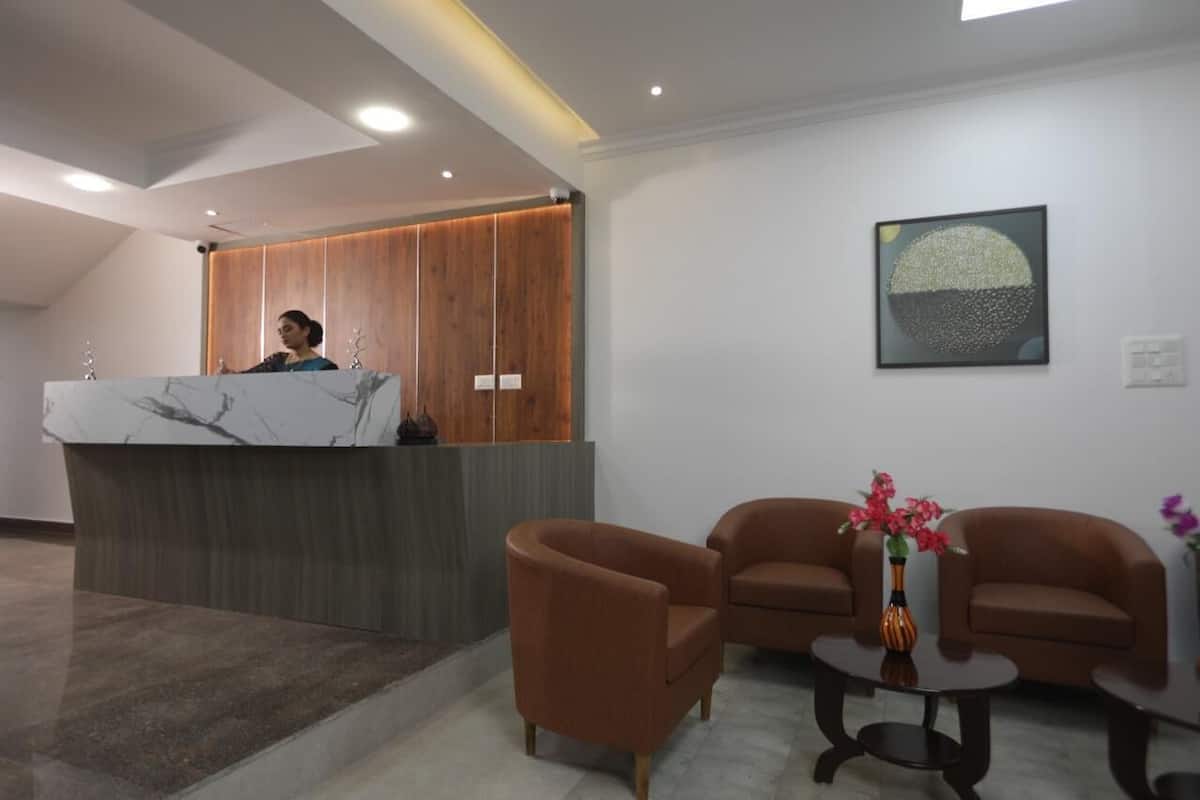 Un área de recepción con mostrador de mármol, panel de madera de fondo, dos sillones marrones, una mesita con un florero y una obra de arte colgada en la pared.