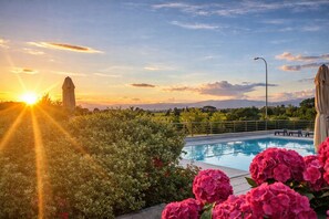 Une piscine avec vue sur le coucher de soleil, entourée de verdure et agrémentée d’une statue.
