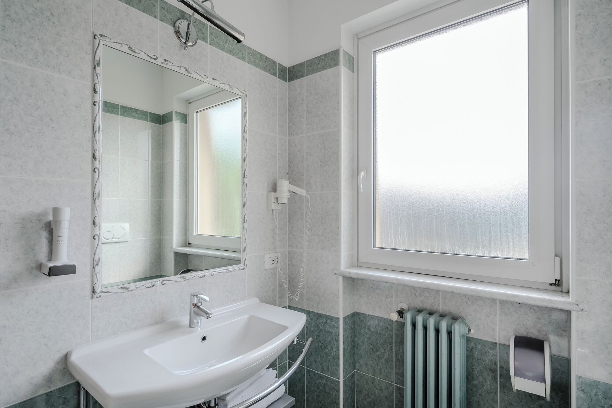 A bathroom with a white sink, a mirror, and a window with frosted glass.