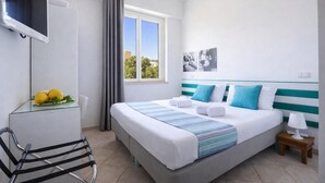 Una habitación de hotel con una cama, un televisor, una silla, un ventanal y una mesita de noche con una lámpara.