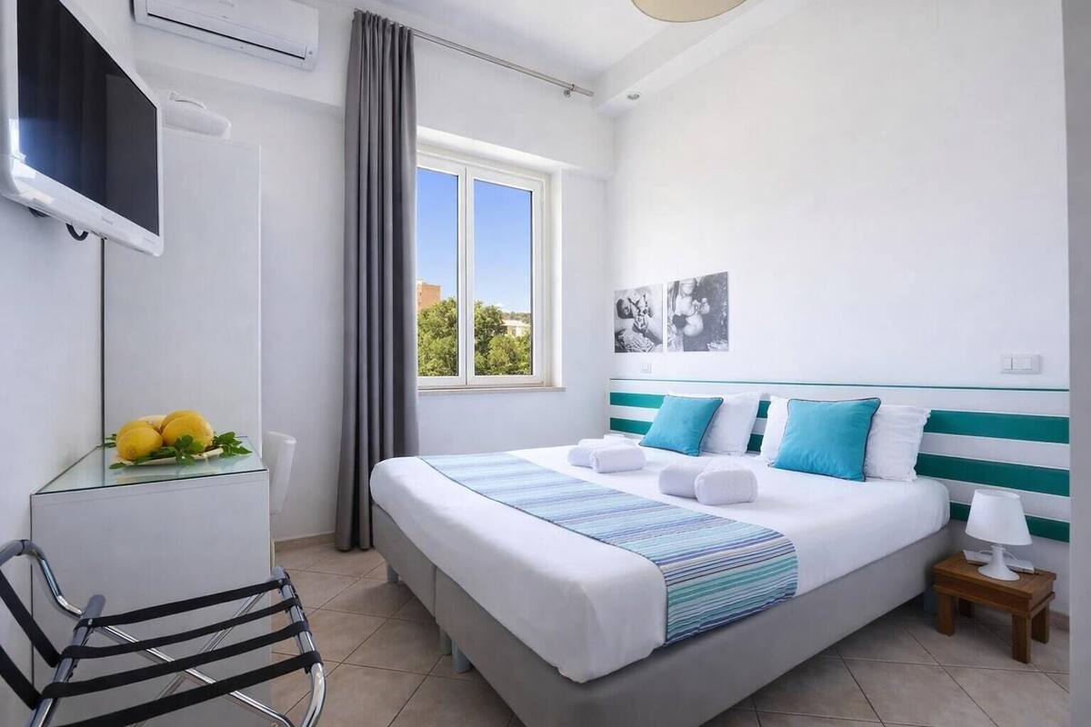 Een hotelkamer met een bed, een televisie, een stoel, een raam en een klein tafeltje met een lamp.