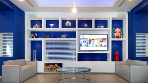 Un área de recepción moderna con una mesa de vidrio central, decoración azul y blanca y una pantalla digital en la pared.