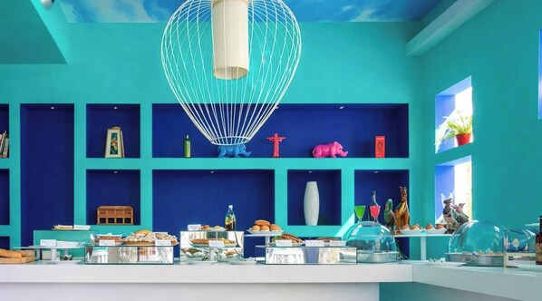 A brightly colored room with teal walls, a central hanging light fixture, and shelves displaying various items including figurines and decorative objects. - Hotiday Capo di Sorrento (Sorrento)