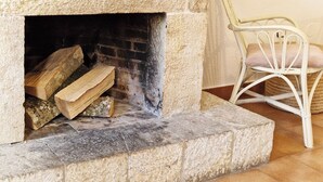 A stone fireplace with logs, a white wicker chair, and a wooden bench. - Apartment 3 (Pido)