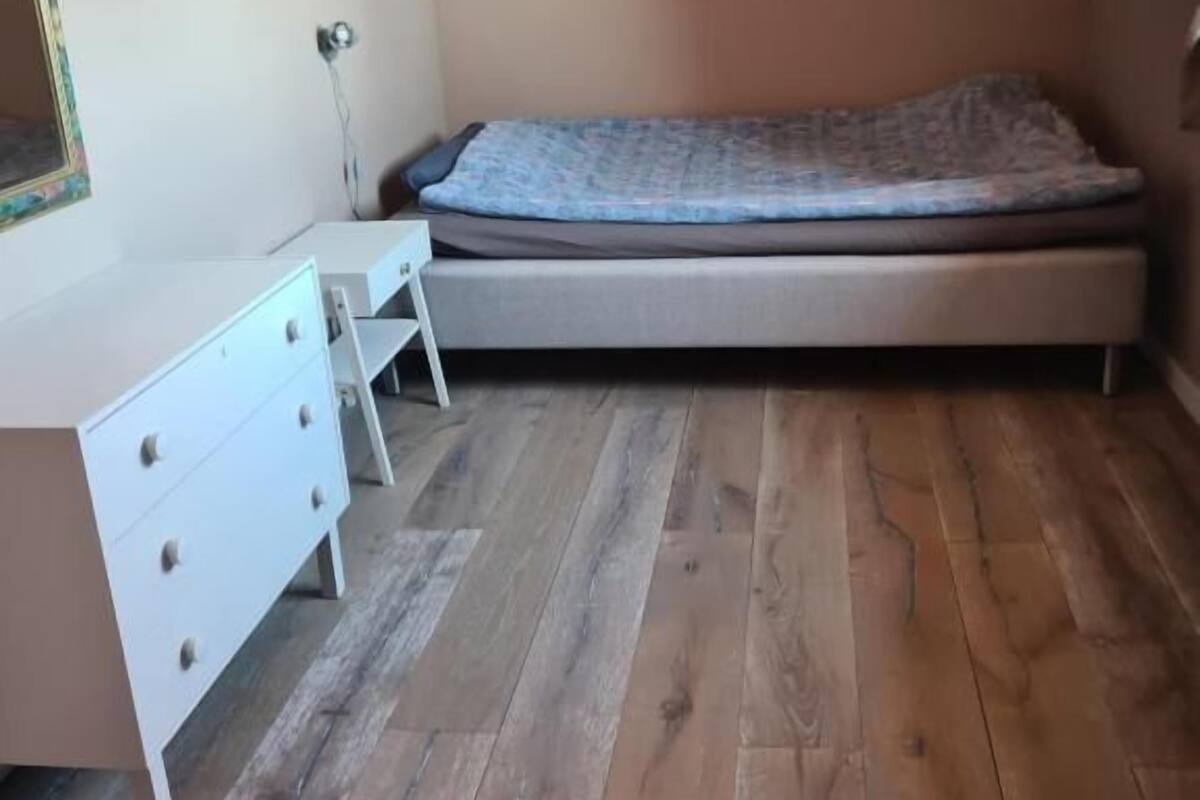 Un dormitorio con una cama, un aparador blanco con cajones y una mesita.