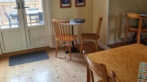 A dining area with wooden chairs and a table, a door leading outside, and a wall with framed pictures and a poster.