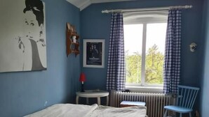 A bedroom with a bed, a window with curtains, a radiator, and a chair.