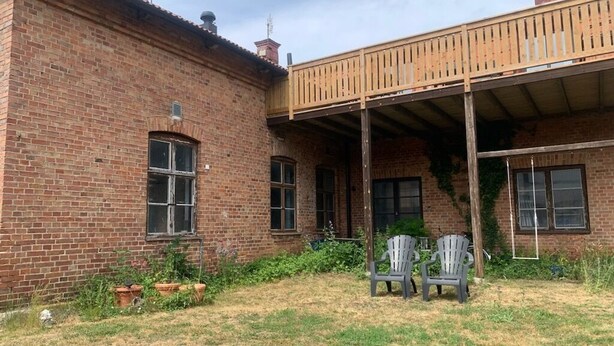A brick building with a wooden balcony, two chairs, and potted plants.