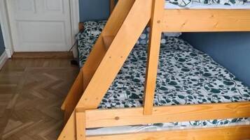 Una cama litera con estructura de madera y ropa de cama estampada en una habitación con suelo de espiga y una puerta blanca.
