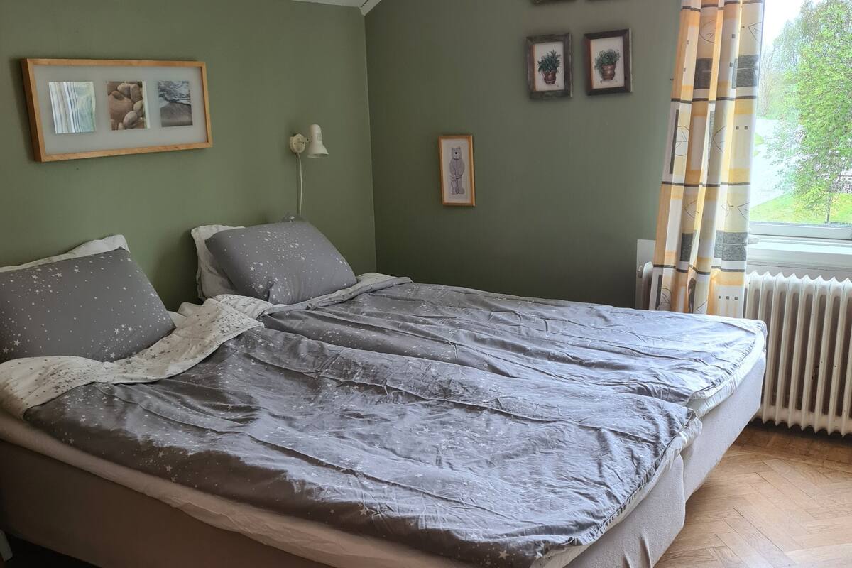 Un dormitorio con cama, radiador y ventana con cortinas.