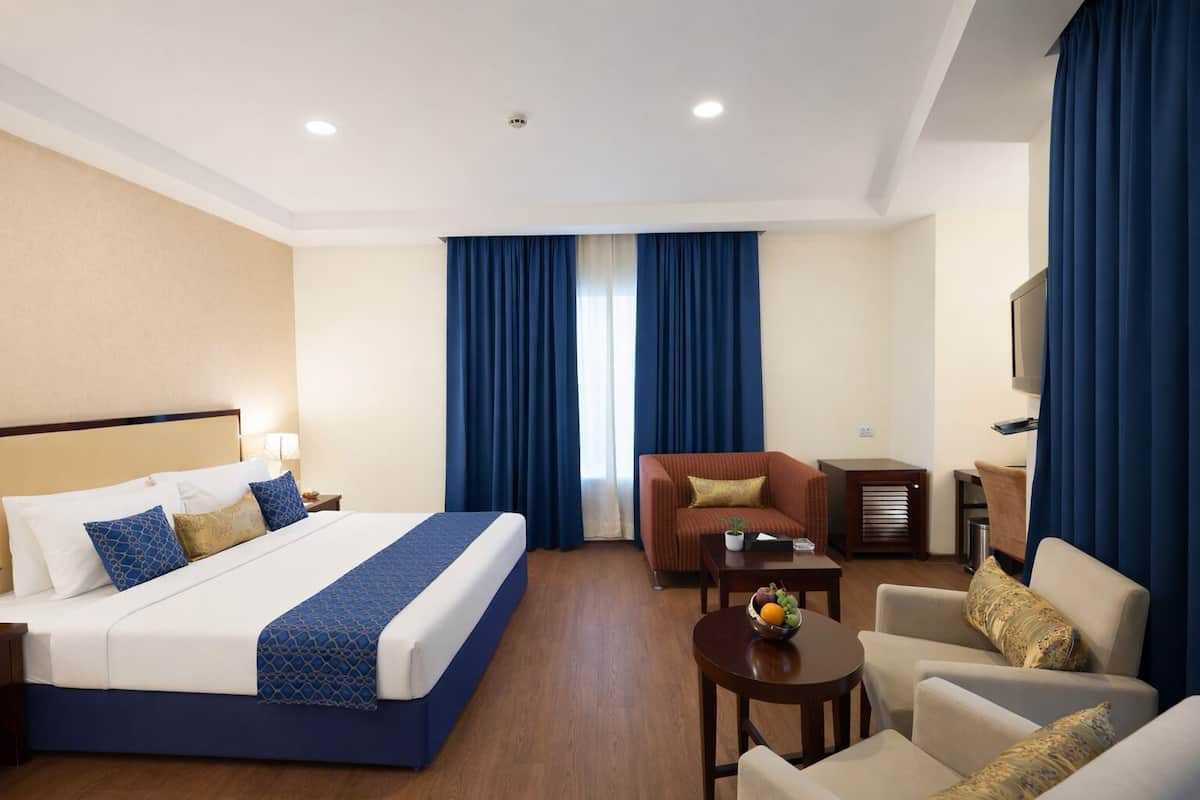 Habitación de hotel con una cama grande, dos sillones, una mesita con fruta y un televisor.