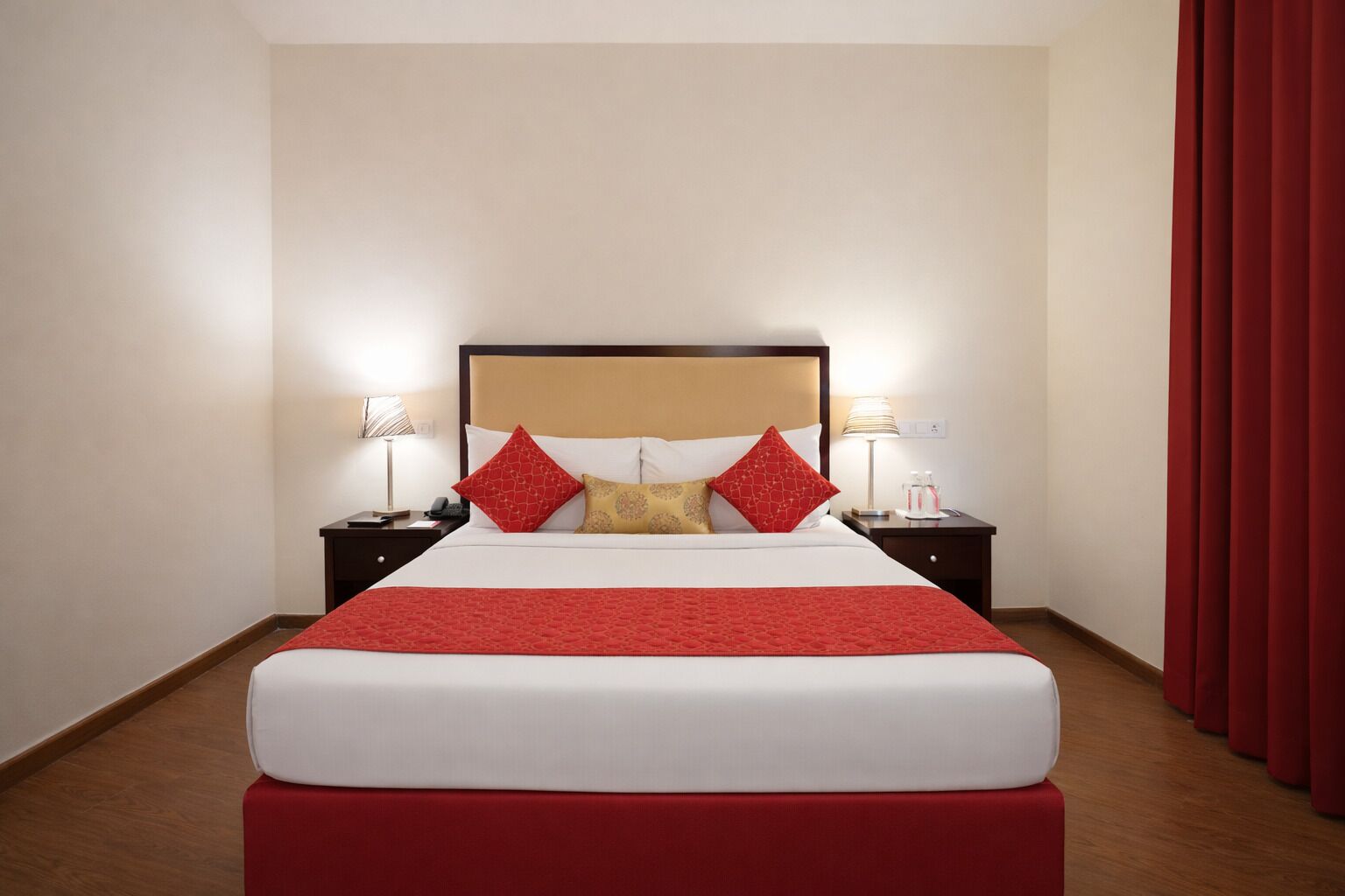 Una habitación de hotel con una cama grande, dos mesitas de noche con lámparas y una cortina roja.
