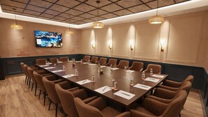 A conference room with a long table, brown chairs, and a large screen on the wall. - Hotel Amber Palace (Gurugram)