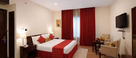 A hotel room with a bed, bedside tables, a desk, a chair, a television, and a window with curtains.