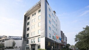 A multi-story hotel with a modern facade, a prominent sign for Hotel Amber Palace, and multiple flags displayed outside. - Hotel Amber Palace (Gurugram)