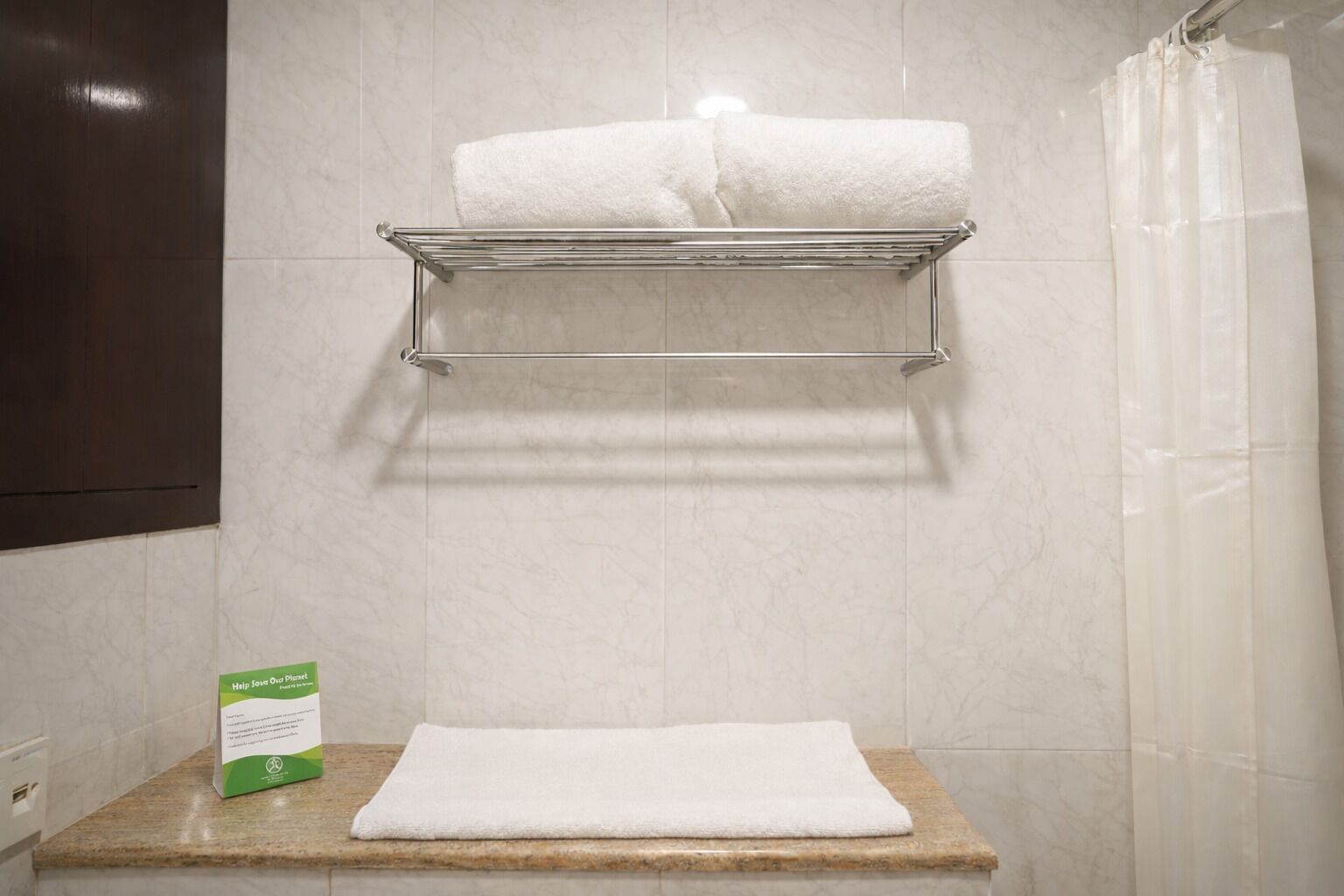 A bathroom with a towel rack holding two white towels, a shower curtain, and a green sign on the countertop.