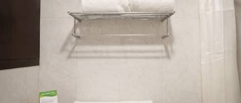 A bathroom with a towel rack holding two white towels, a shower curtain, and a green sign on the countertop.
