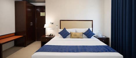 A hotel room with a large bed, a bedside table with a lamp, a nightstand, a bench, and a wardrobe.