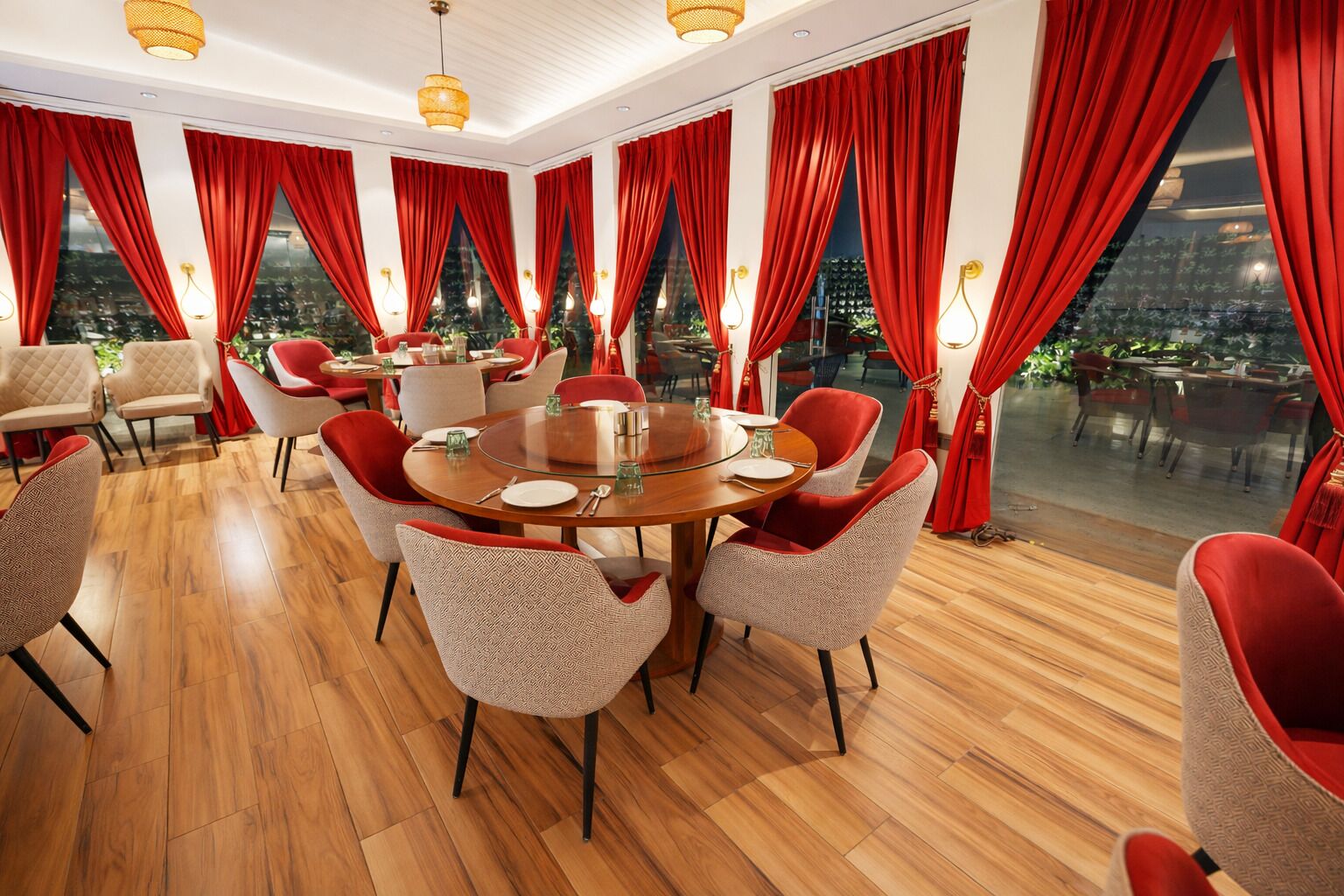 Un comedor con una mesa redonda, cortinas rojas y suelo de madera.