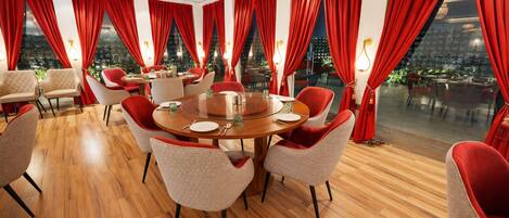 Un comedor con una mesa redonda, cortinas rojas y suelo de madera.