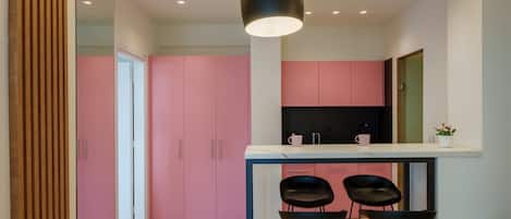 Una cocina moderna con armarios rosados y encimera blanca. Hay tres taburetes negros debajo de una lámpara colgante.