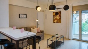 A modern living room with a white marble table, black chairs, a glass coffee table, a sofa with cushions, and a painting on the wall. - Irakleio Notos Boutique Apartments 2 (Heraklion)
