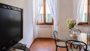 Een kamer met een televisie, een glazen tafel met stoelen, een raam met gordijnen en een radiator.