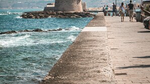 A coastal walkway with a lighthouse, rocky shoreline, and people walking. - Irakleio Notos Boutique Aprtmnts 3 Private Jacuzzi (Heraklion)