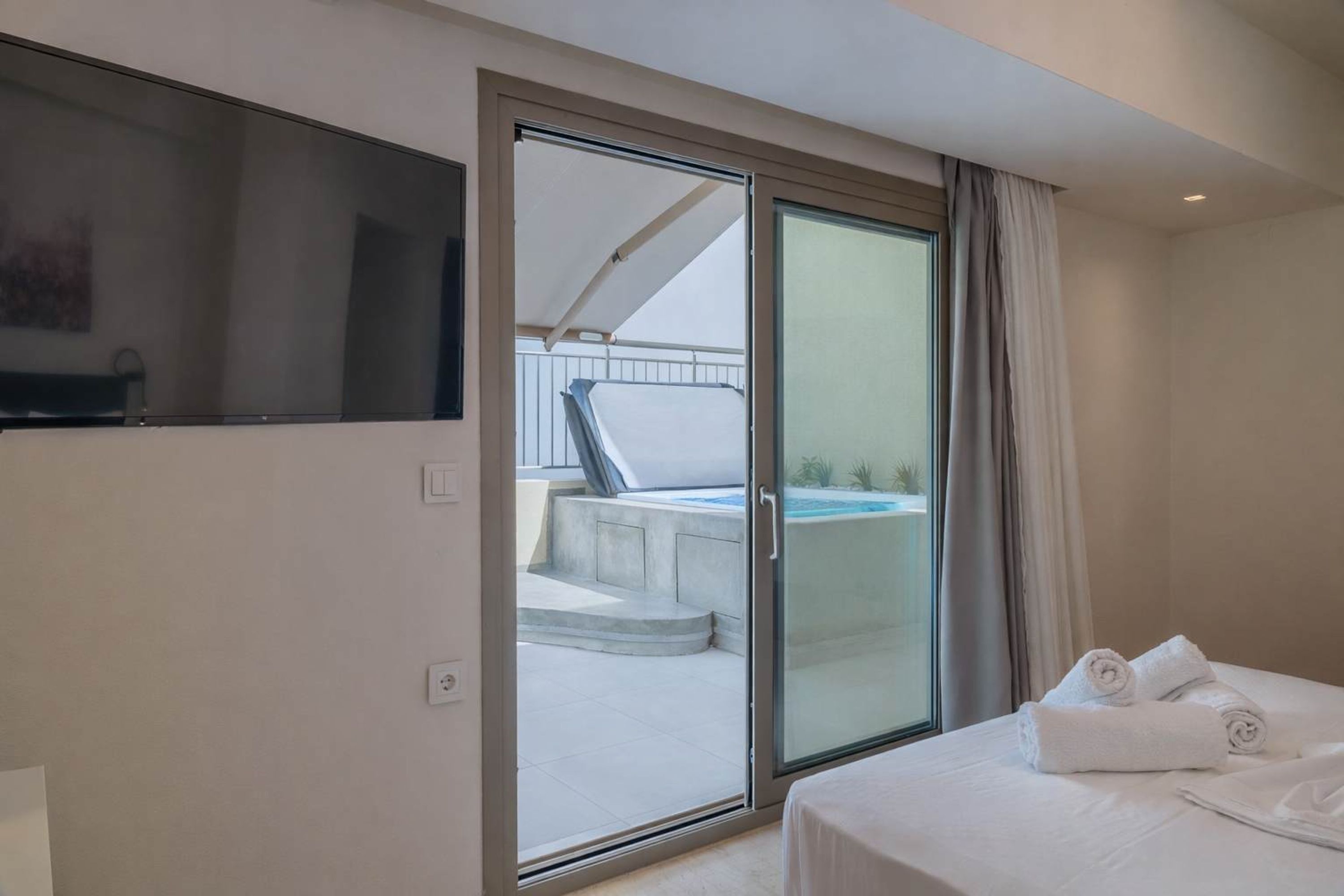 A hotel room with a bed, a TV, a sliding glass door leading to a balcony with a hot tub.