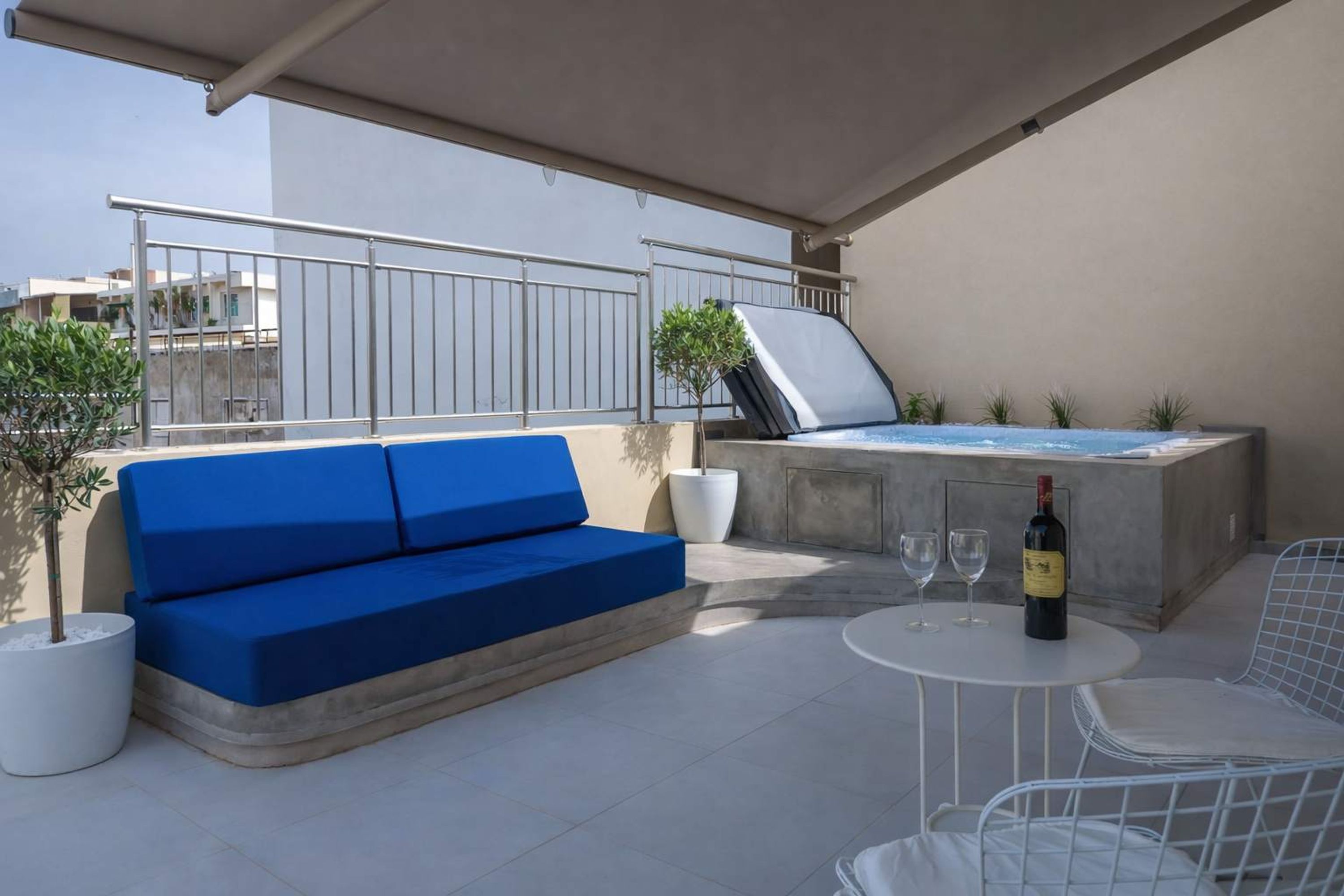 Een terras op het dak met een blauwe bank, een jacuzzi, een tafel met twee wijnglazen en een potplant.