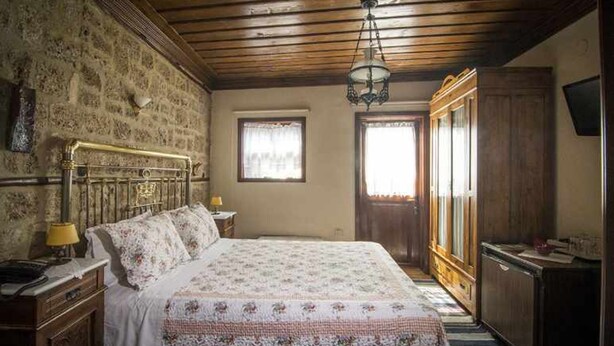 A bedroom with a wooden headboard, a bed with floral bedding, a nightstand, a dresser, and a television on the wall. - Hagiati Karanos - Edessa Cozy Mountain Retreat (Edessa)