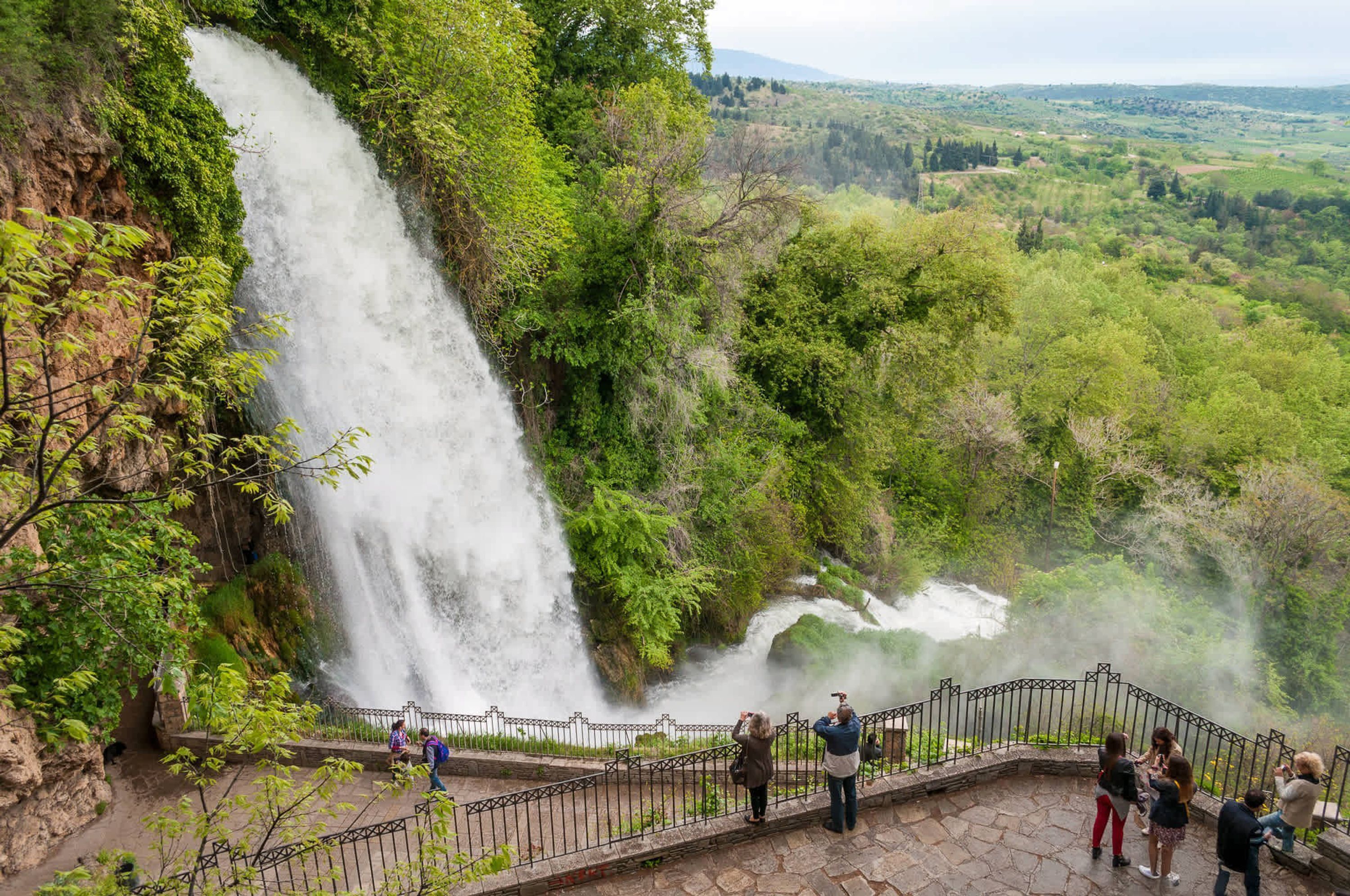 A waterfall cascading down a rocky cliff surrounded by lush greenery.