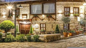 A stone building with a wooden door, multiple windows with curtains, and outdoor seating with potted plants. - Hagiati Karanos - Edessa Cozy Mountain Retreat (Edessa)