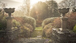 A garden pathway flanked by stone urns, leading to a lush green area with trees and shrubs. - Whitbarrow Lodge Ridgestone (Grange-over-Sands)