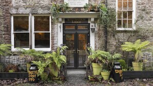 A stone building with a sign reading "Whitbarrow Lodge" and a door with glass panels. There are potted plants in front of the door. - Whitbarrow Lodge Ridgestone (Grange-over-Sands)