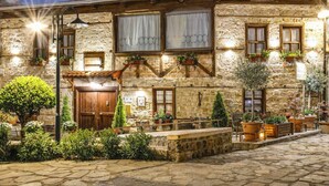 A stone building with a wooden door, multiple windows with curtains, and outdoor seating with potted plants. - Hagiati Filippos - Edessa Cozy Mountain Retreat (Edessa)
