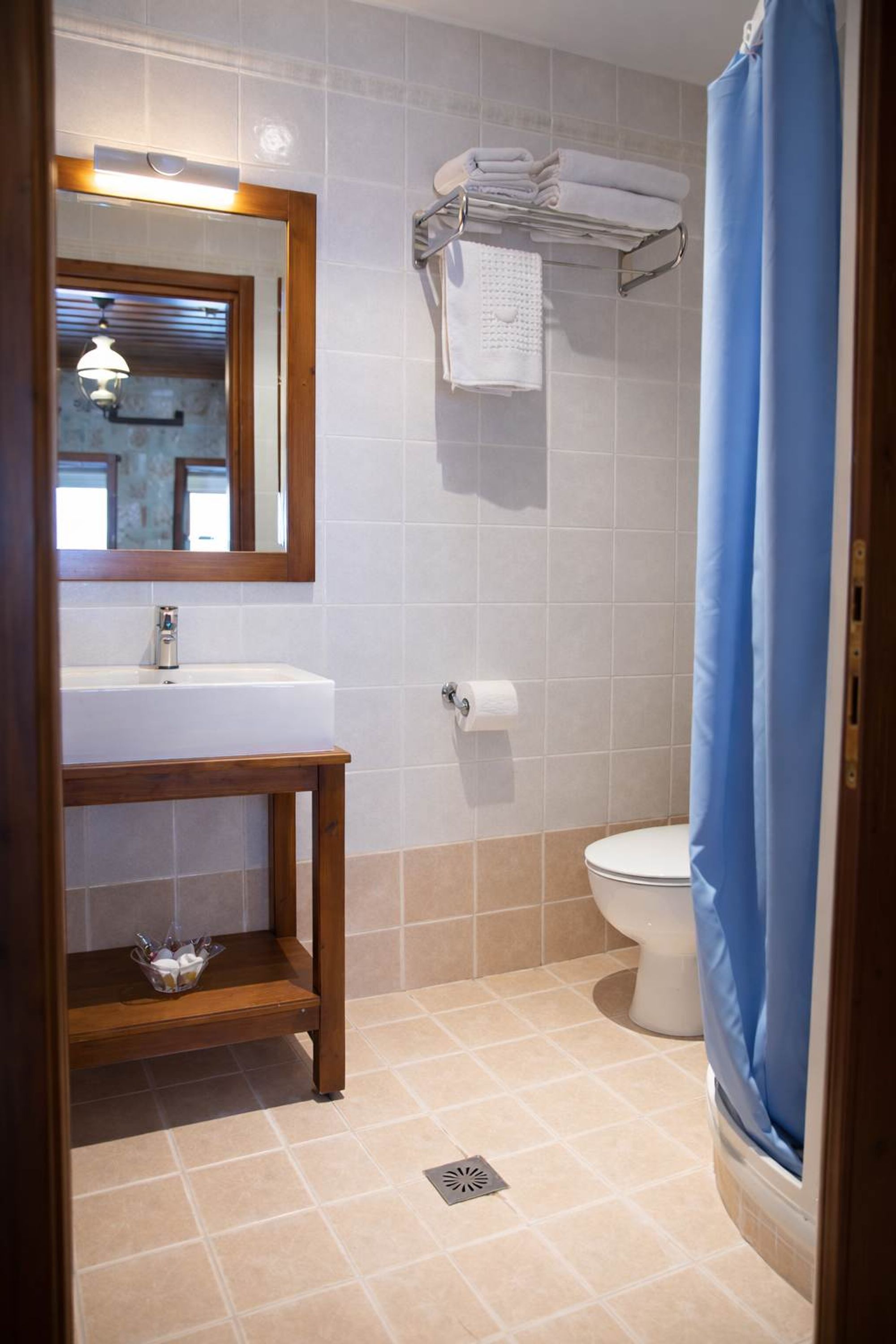 A bathroom with a sink, mirror, towel rack, toilet, and shower curtain.