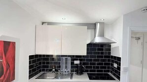 A compact kitchen with a black tiled backsplash, white cabinets, a stainless steel range hood, and a built-in oven. - Entire Flat in Greater London, United Kingdom (London)
