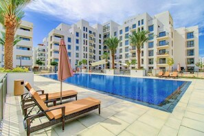 Ein modernes Hotel mit großem Pool, Liegestühlen und Palmen.