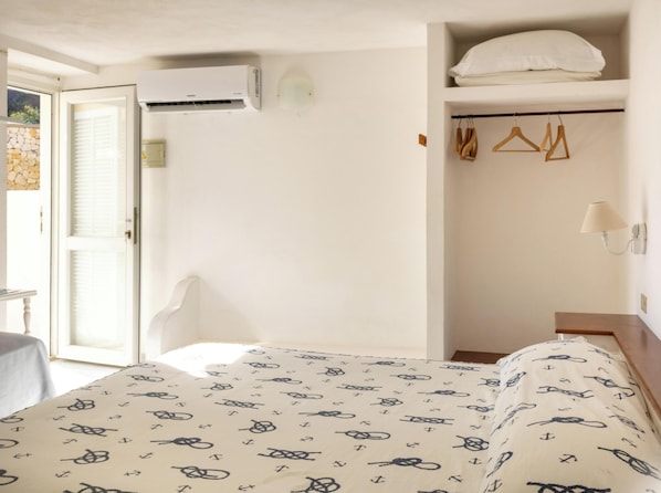 A hotel room with a bed, a wardrobe, a hanging light, and an air conditioning unit.