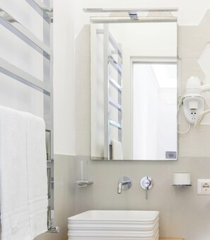 A modern bathroom with a white sink, a mirror, a towel rack, a hairdryer, and a toilet paper holder.