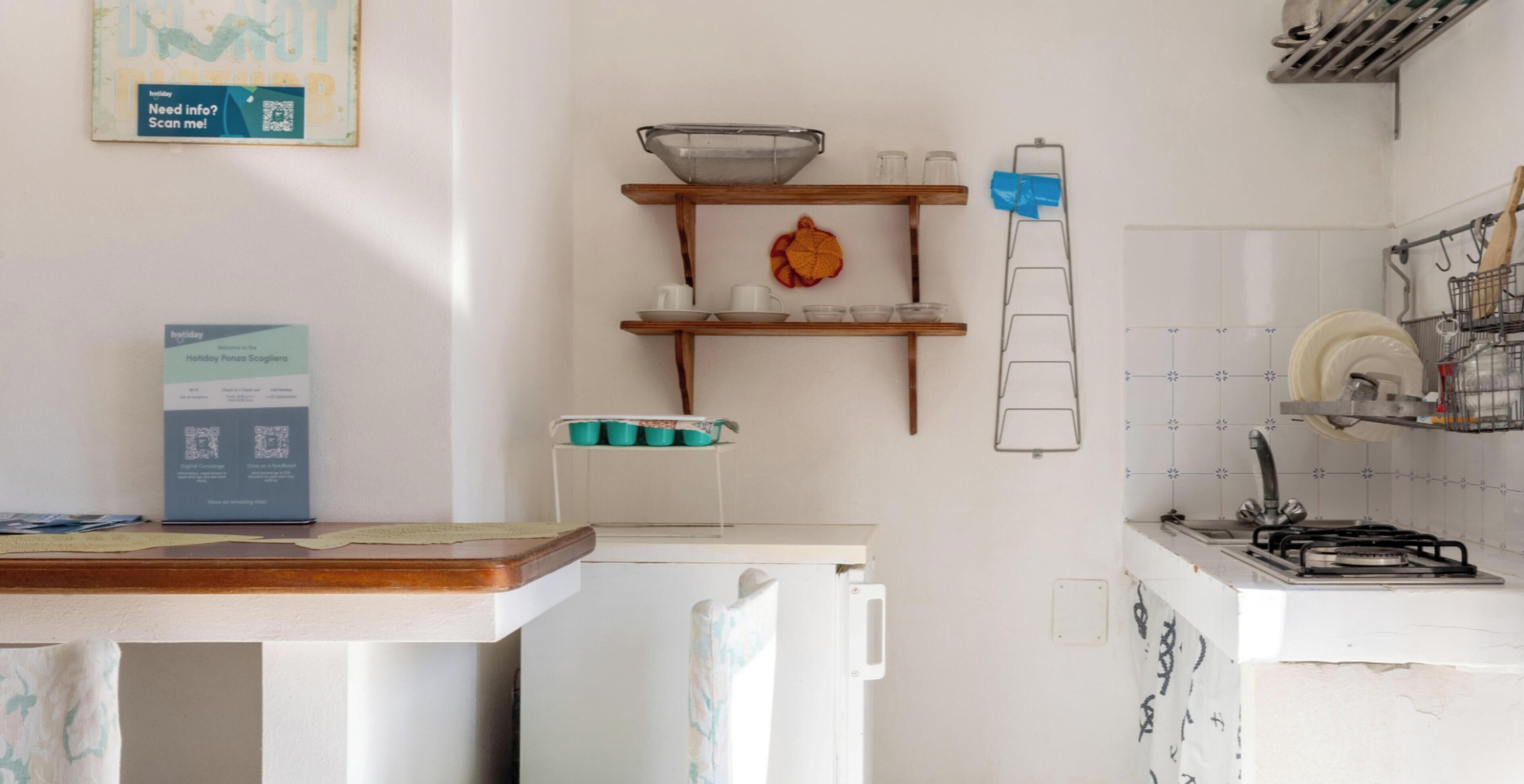 Una cocina con refrigerador, pileta, estufa y una alacena con vasos y un objeto decorativo.
