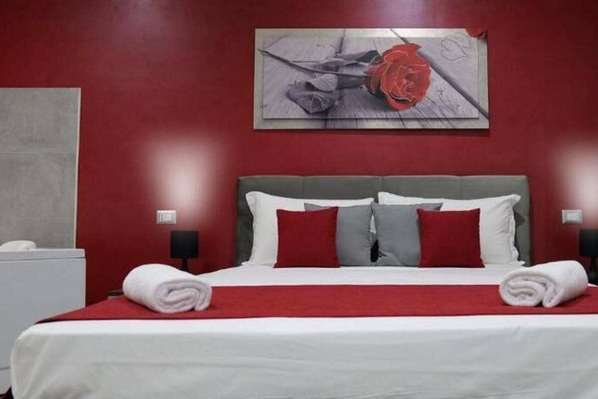 A hotel room with a large bed, red and white bedding, a grey headboard, and a red and white rose painting on the wall.
