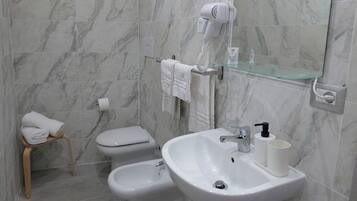 Une salle de bain avec un mur en marbre, des toilettes, un bidet, un lavabo avec un miroir et un sèche-cheveux fixé au mur.