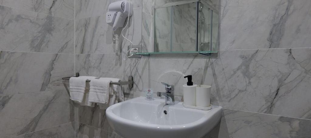 A bathroom with a marble sink, a hairdryer, and a glass shelf.